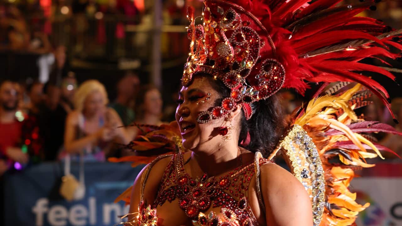 A person dressed in a red and yellow embellished costume, a matching crown and feathers.