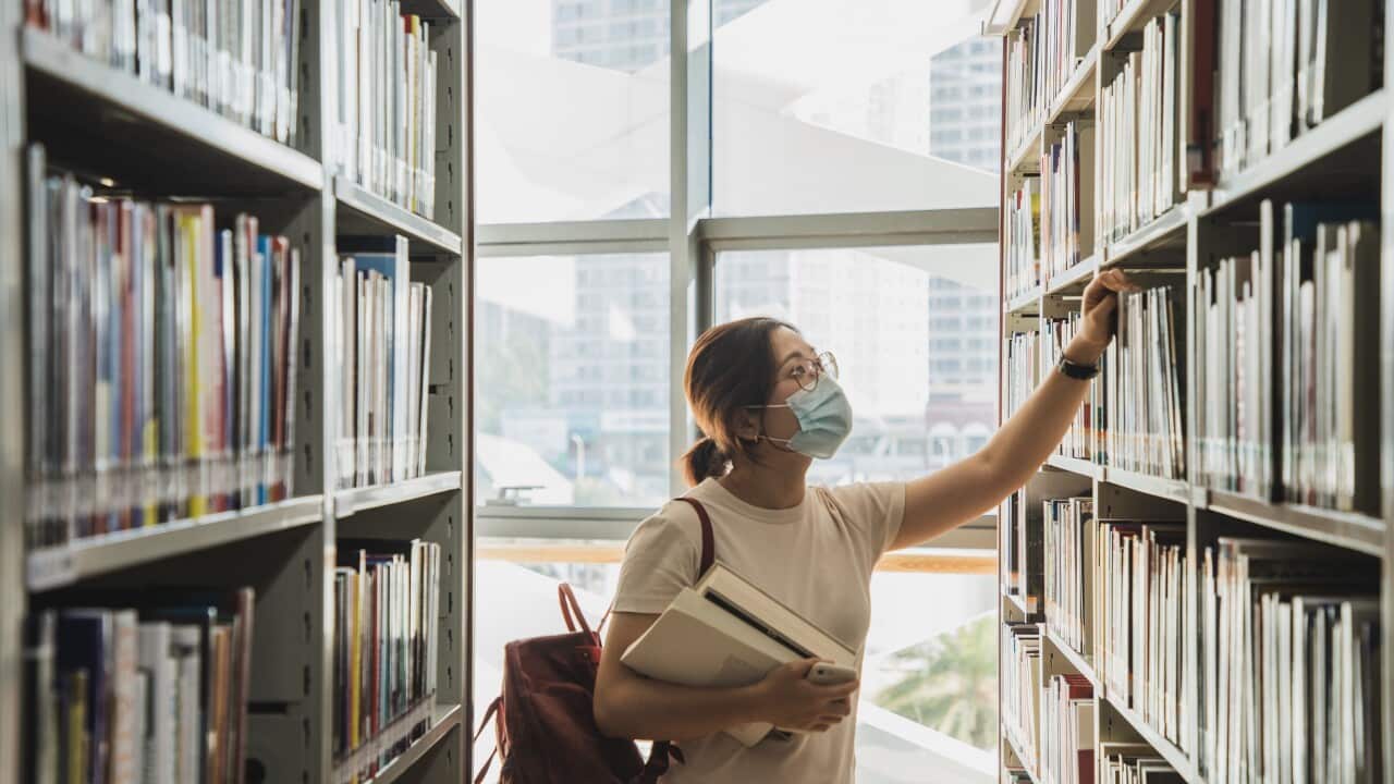adult student wearing face mask looking at the books from the bookshelf