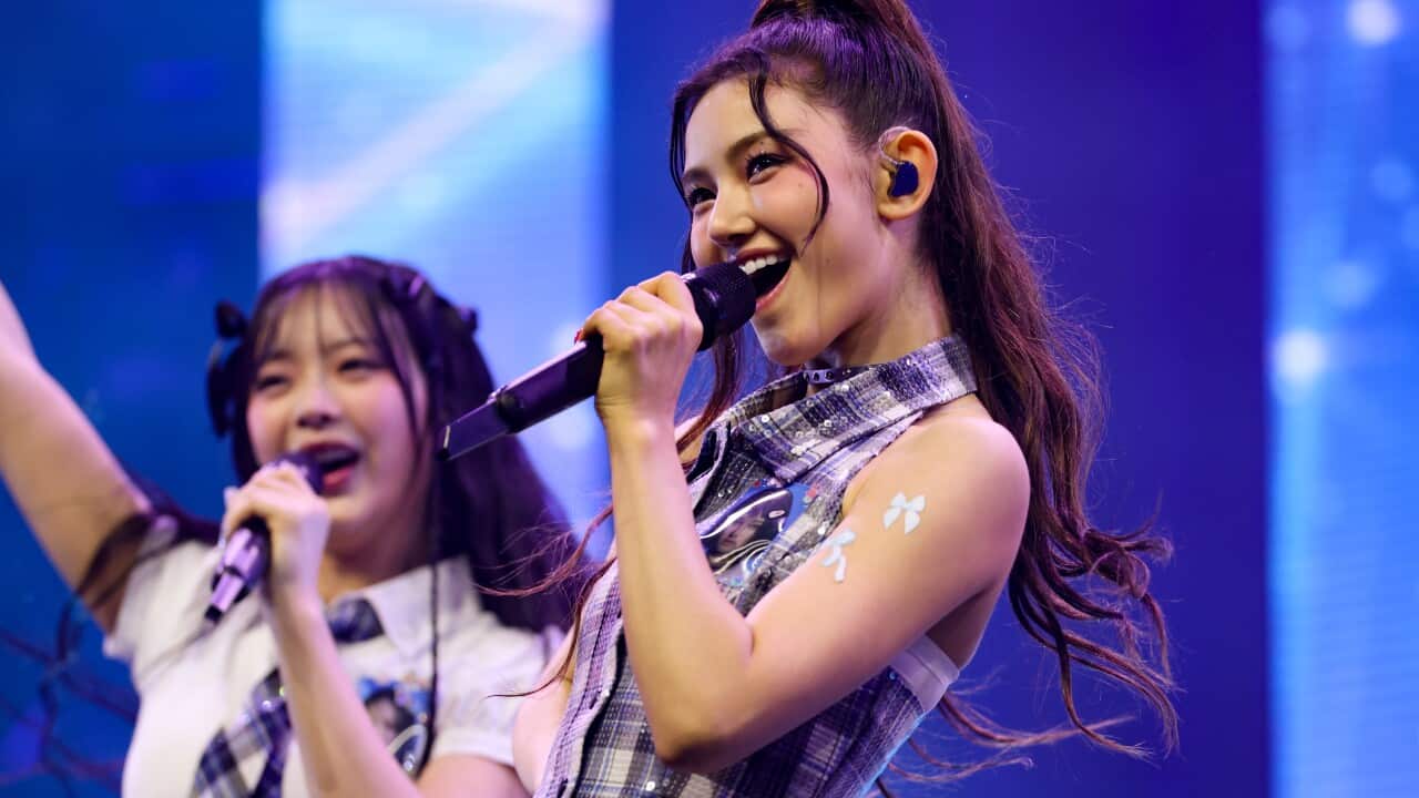 Two young women are singing into microphones in front of a blue background.