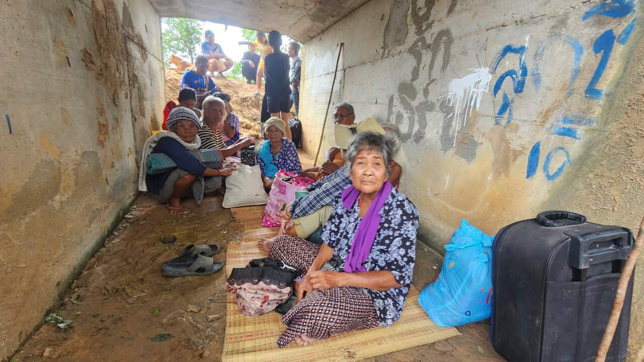People sitting on the ground, inside a makeshift shelter.