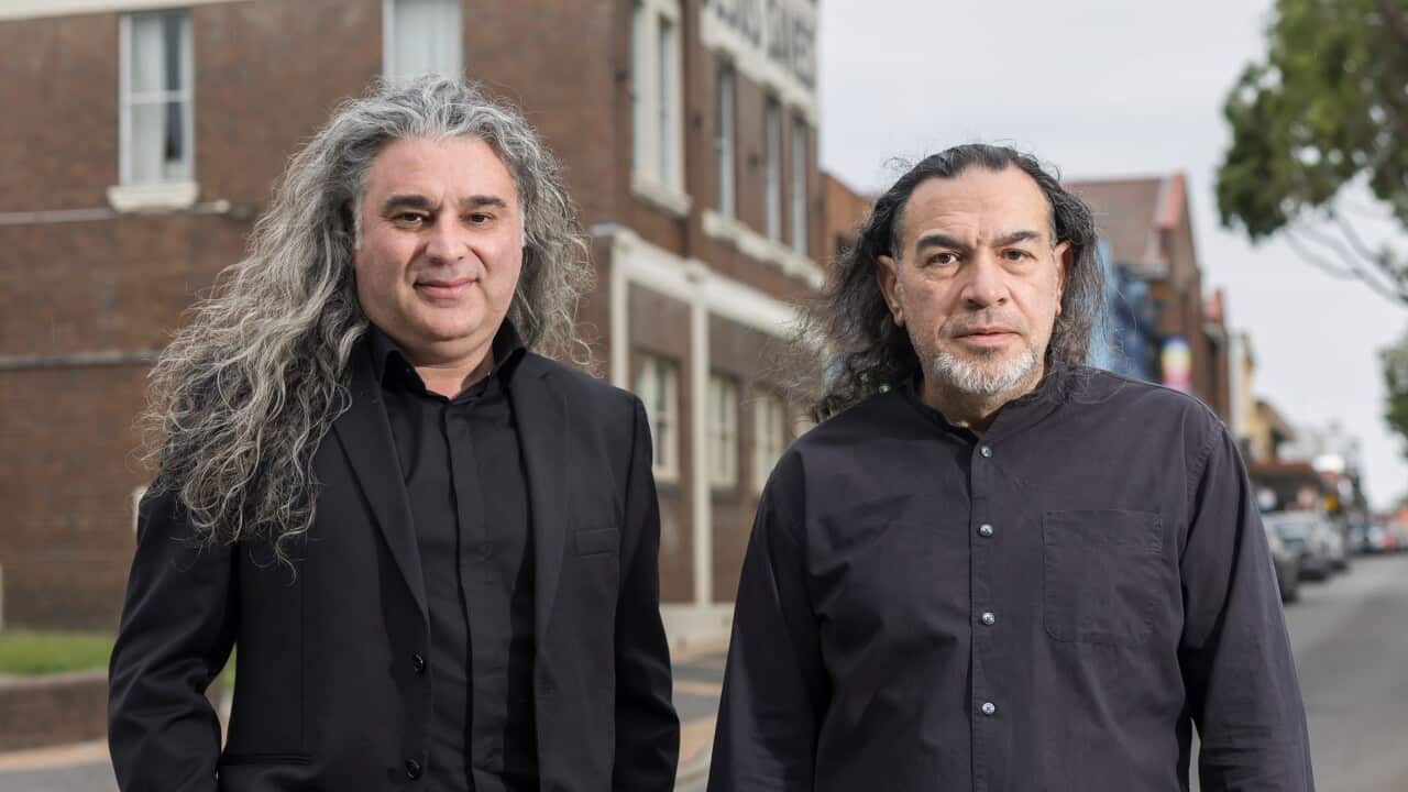 Two men wearing black shirts pose for a photo