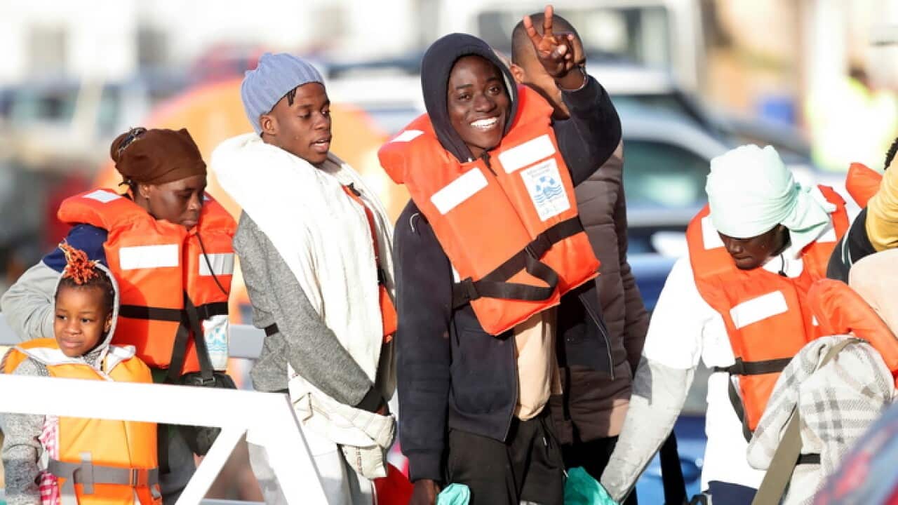 : Migrants wave as they disembark at Pieta, Malta
