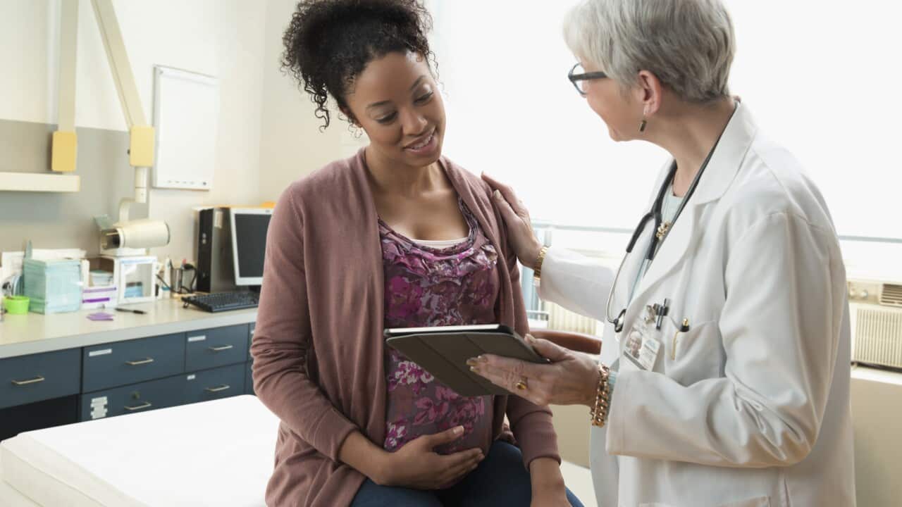 Gynecologist with digital tablet comforting pregnant patient