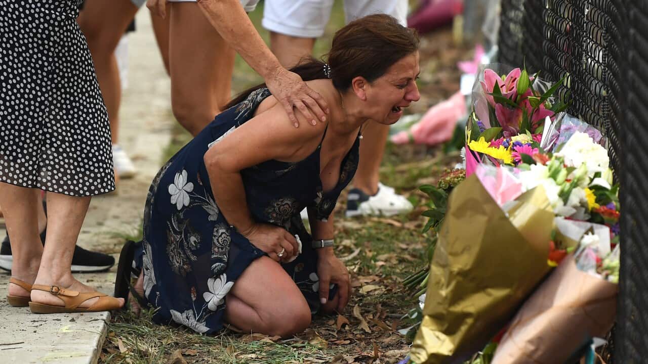 A woman pauses near flowers placed at the scene where seven children where hit on a footpath by a four-wheel drive in the Sydney suburb of Oatlands