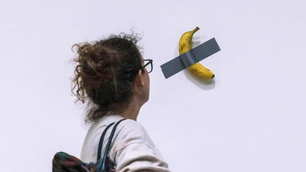 A woman looks at a banana duct taped to a wall.