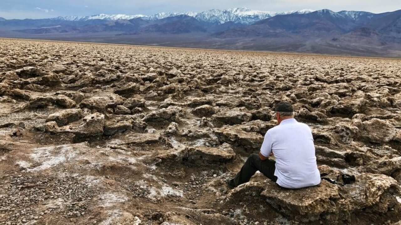 Rear View Of Man Sitting On Rock Against Mountains At Death Valley National Park