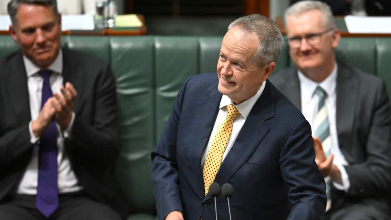 A man in a navy suit and yellow tie, smiling as he looks to his right.