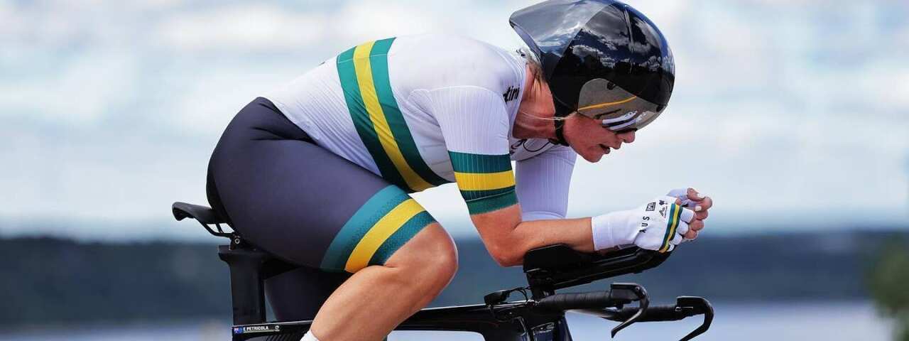 Cyclist in Australian colours sits on black Cervelo time trial bike, with water view out of focus behind.