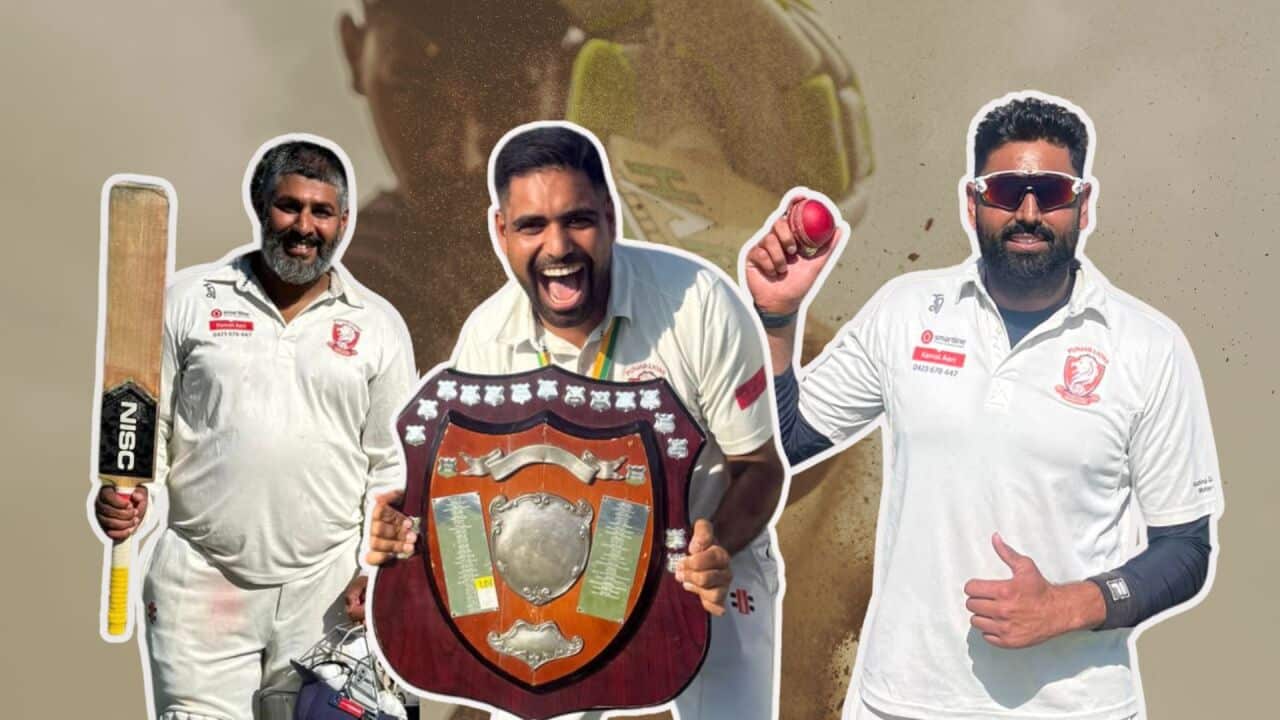 Three cricket players in white uniforms celebrate a victory, with the central player laughing while holding a large championship shield and the others posing with a bat and a cricket ball.