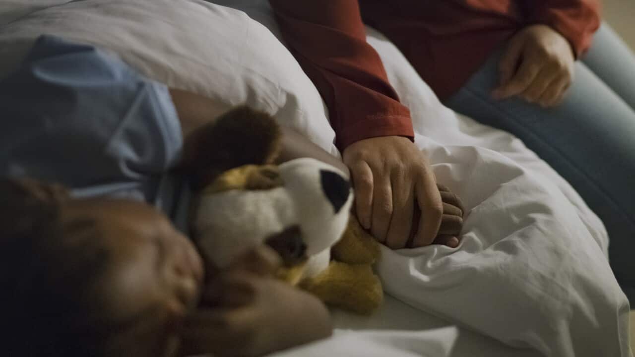 Mother holding ill son's hand sleeping on bed