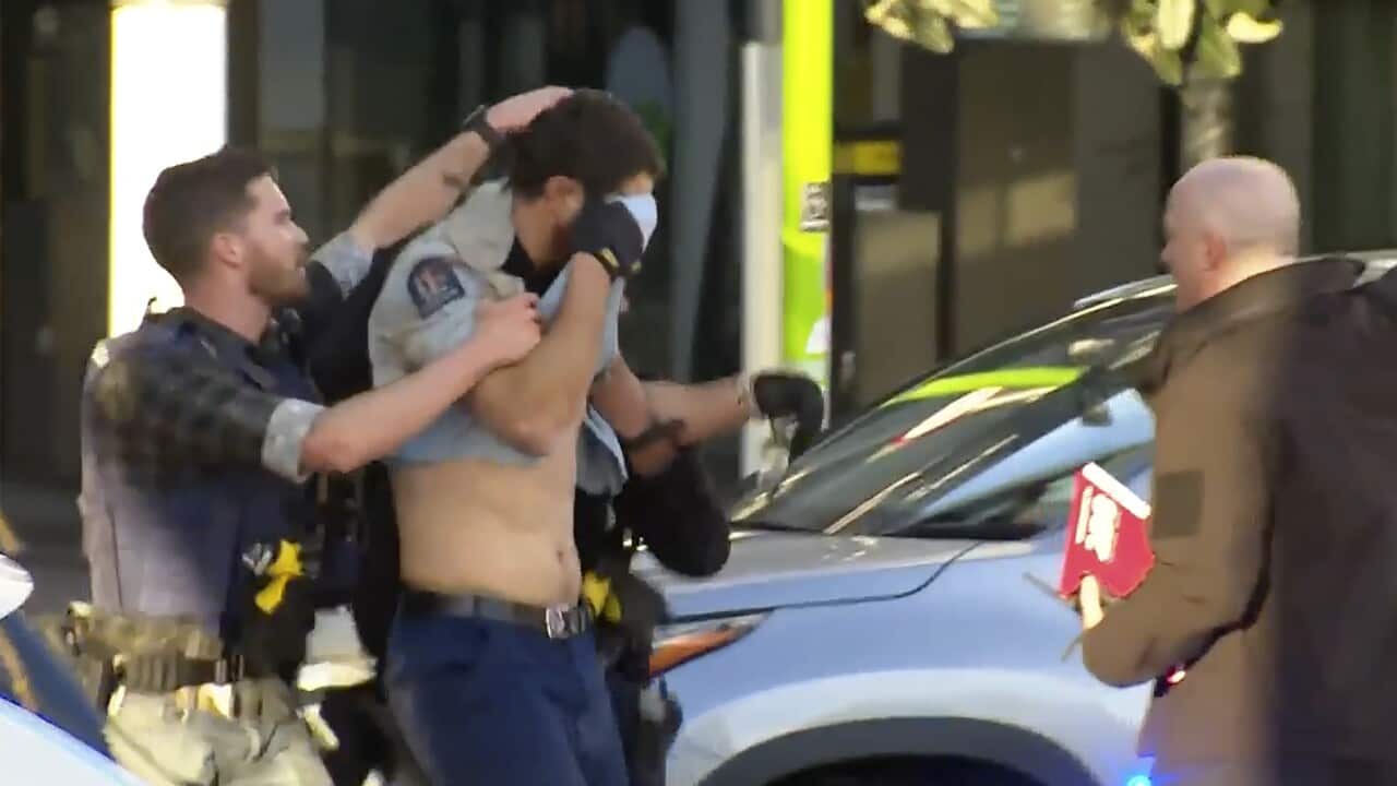 An injured police officer, holding a shirt to his face, is led by another officer