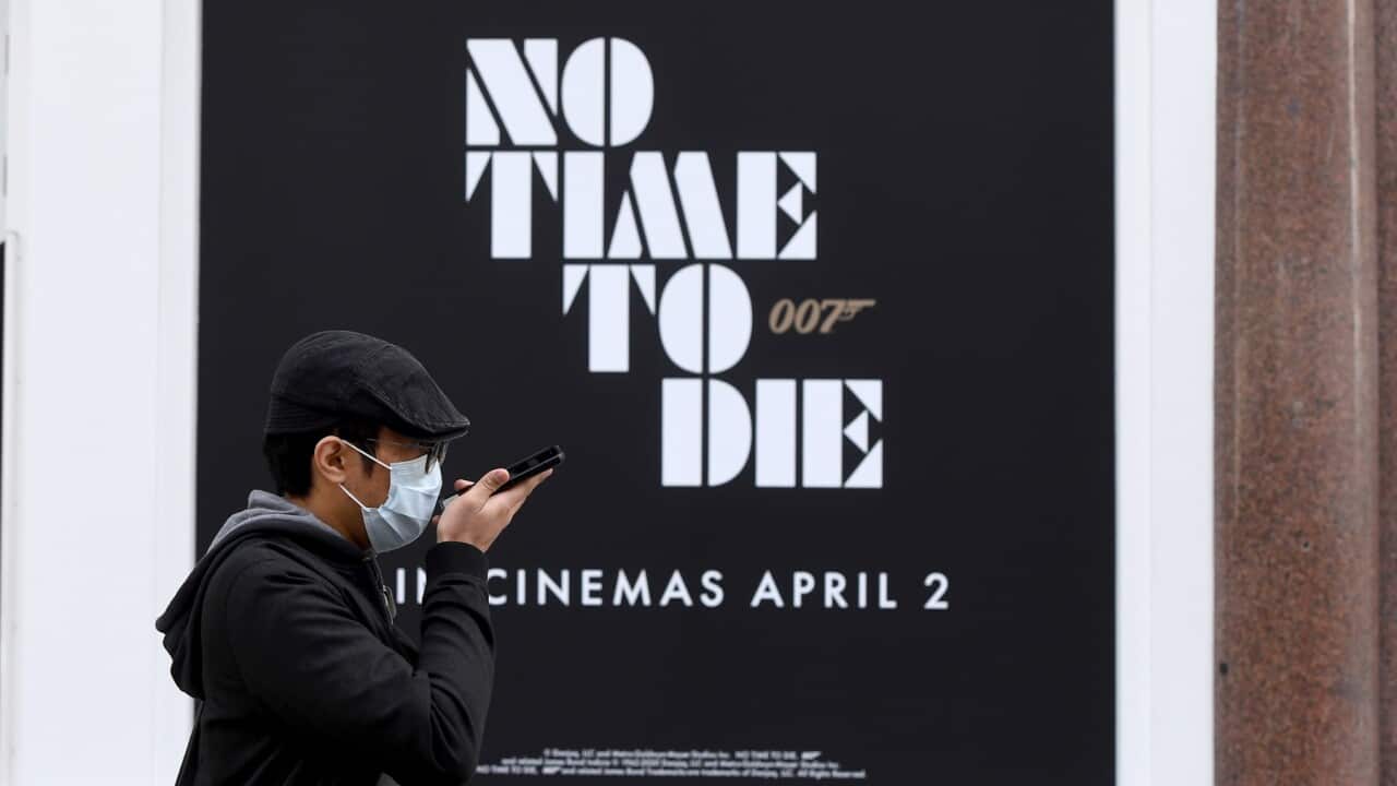 A masked man walks past a new James Bond movie advert in London