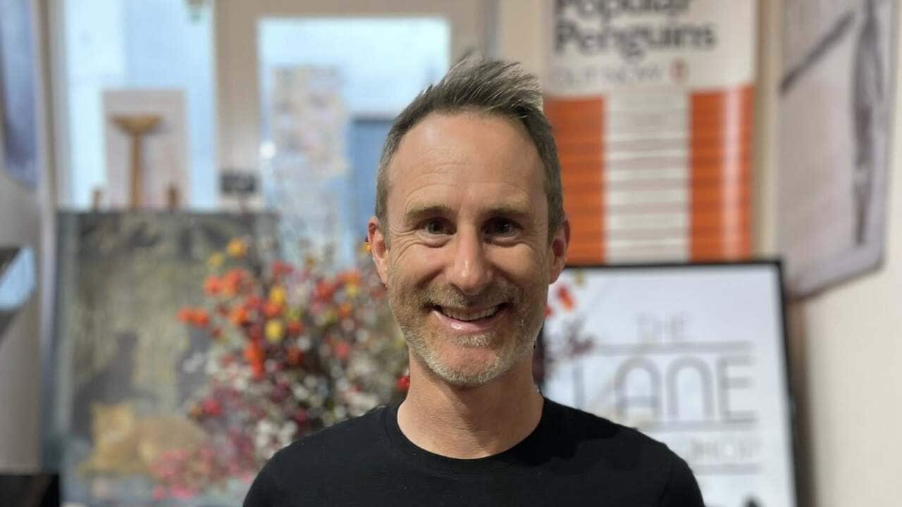 Author Craig Silvey stands in a bookstore smiling while holding two of his books, Runt and Runt and the Diabolical Dognapping.