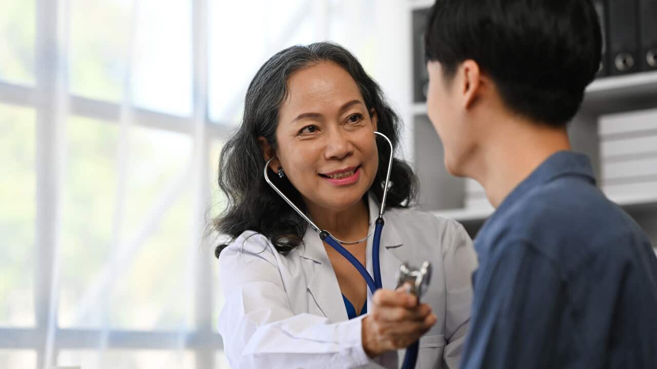 Positive mature doctor using stethoscope, listening to male patient breath or heartbeat. Healthy care concept