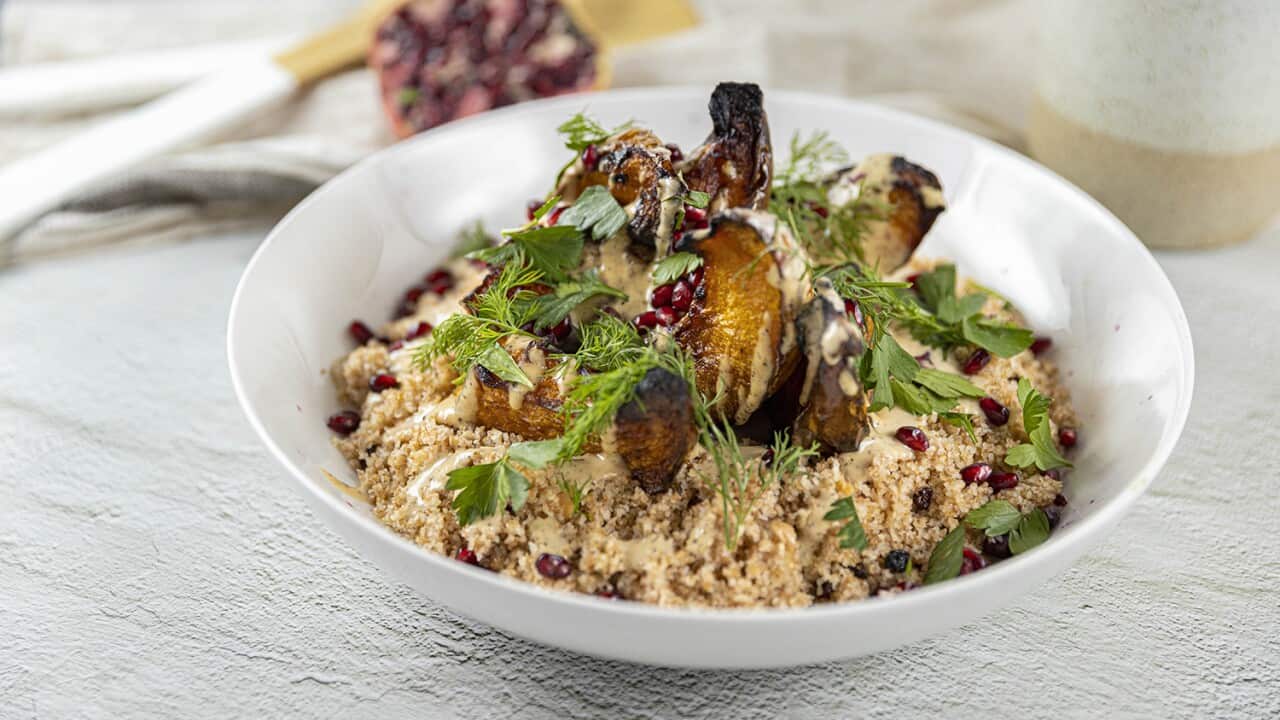 A white bowl holds cooked bulgur topped with pumpkin, herbs and pomegranate seeds.