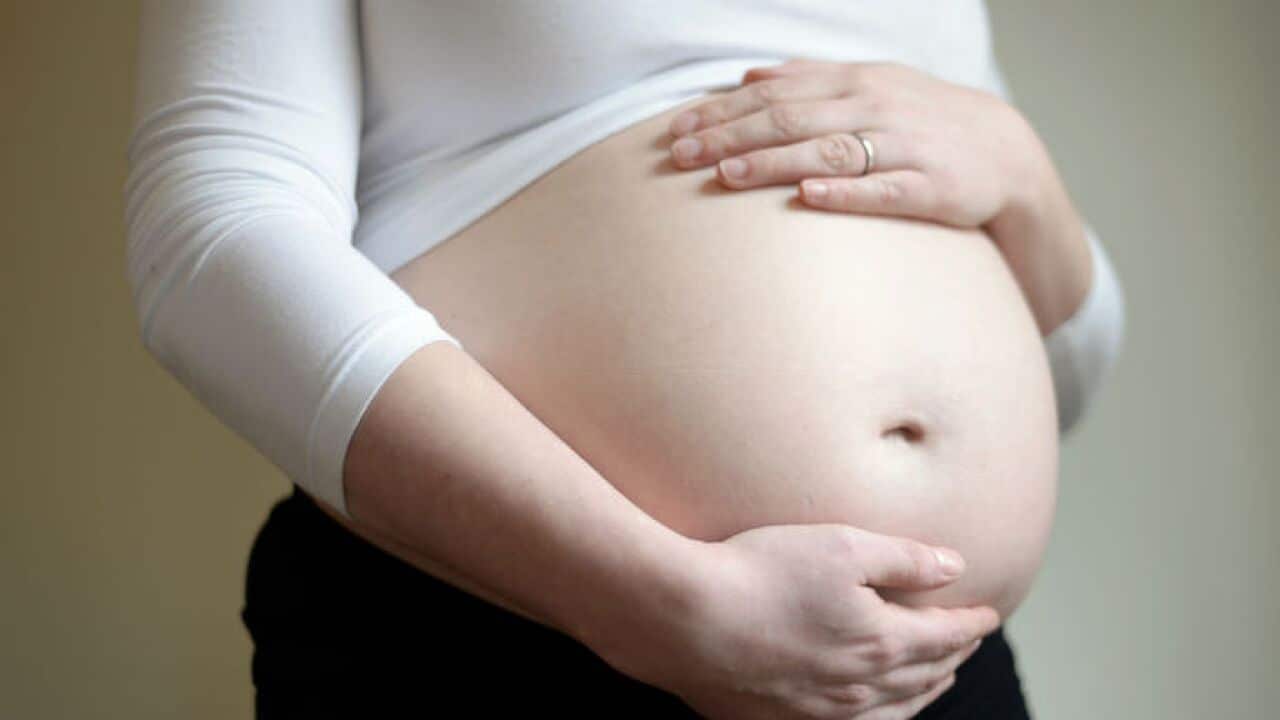 A woamn seven months into her pregnancy holds her stomach