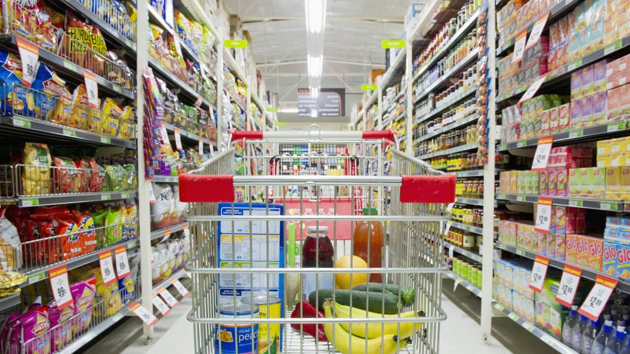 A trolley with groceries inside, in a supermarket aisle.