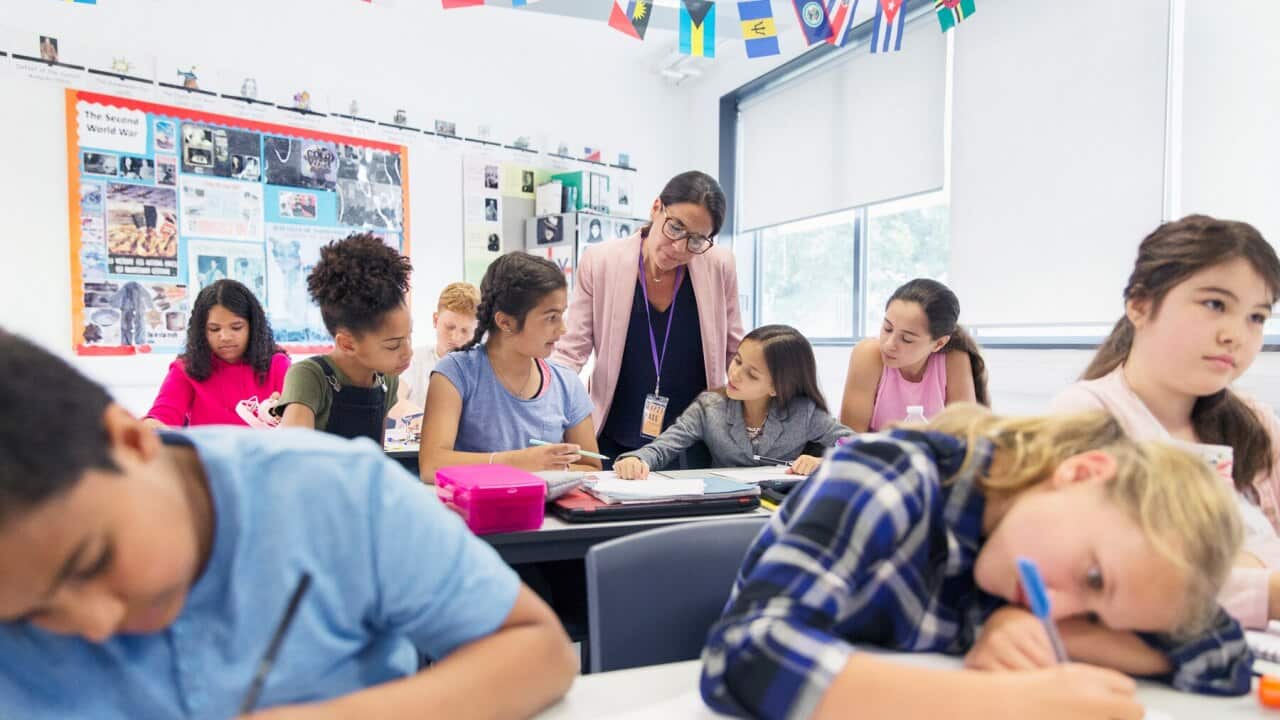 Female teacher helping junior high school girl students doing homework at desk in classroom