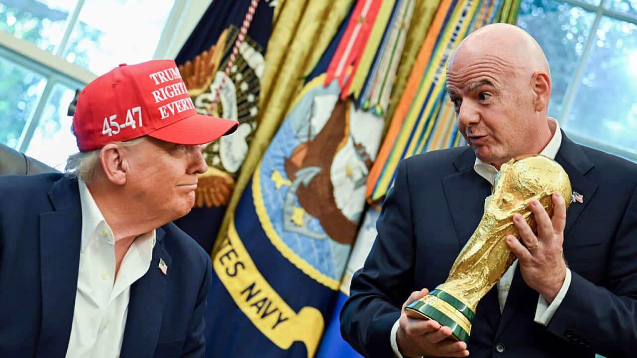 Donald Trump, wearing a red cap reading "Trump was right about everything" sits next to Gianni Infantino, who is standing and holding a gold trophy
