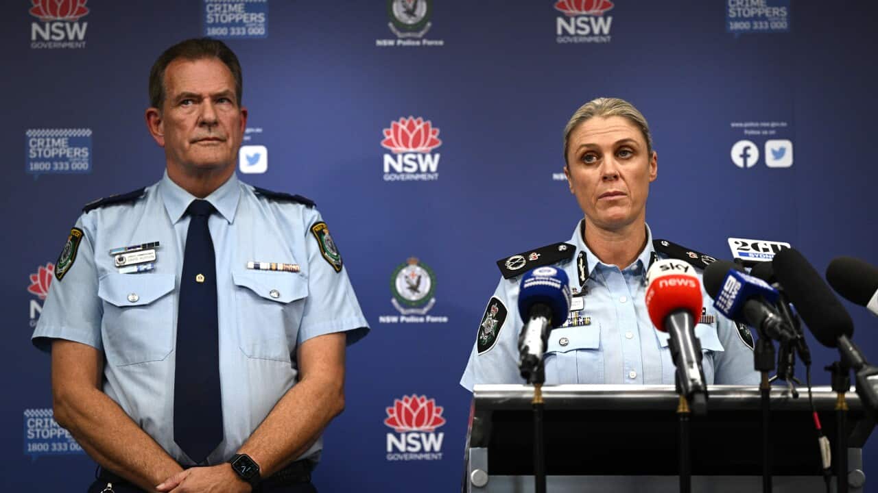 Two police officers stand beside one another in front of a police banner