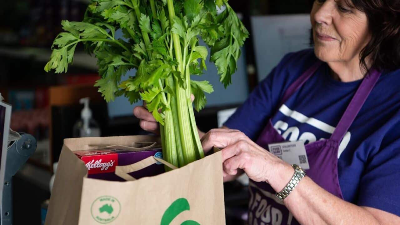 A woman puts celery in her shopping bag.