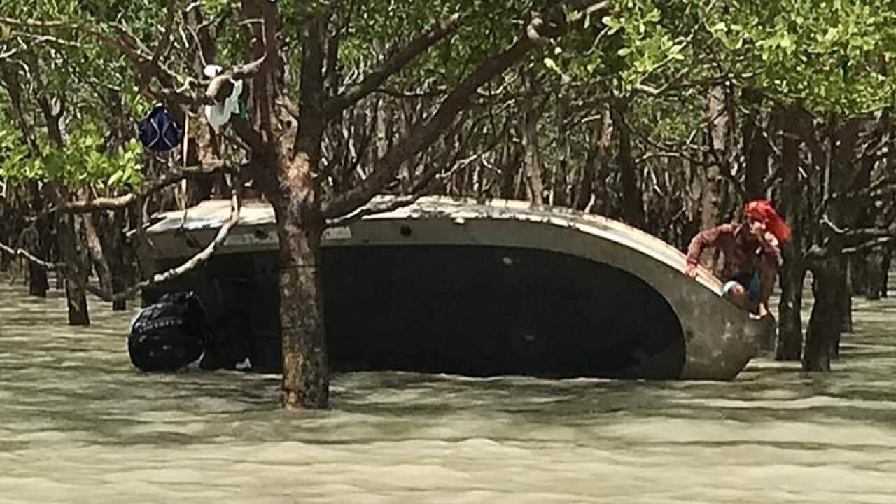 Two men cling onto their overturned tinny.