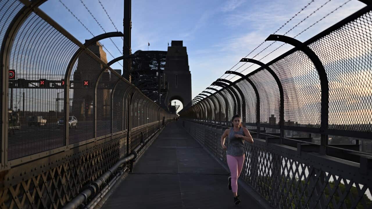 A woman jogs over the Sydney Harbour Bridge at sunrise in Sydney, Thursday, April 2, 2020.