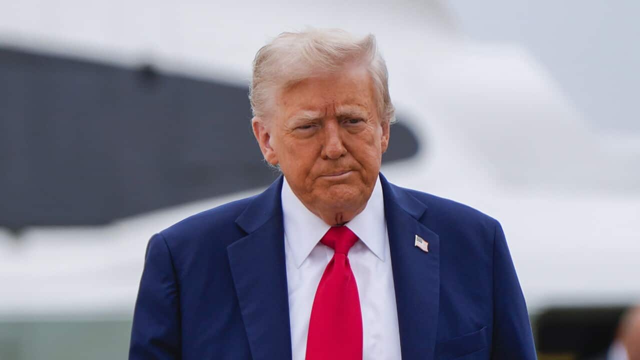 Donald Trump, wearing a blue suit with an American flag pin on it, white shirt and red tie.