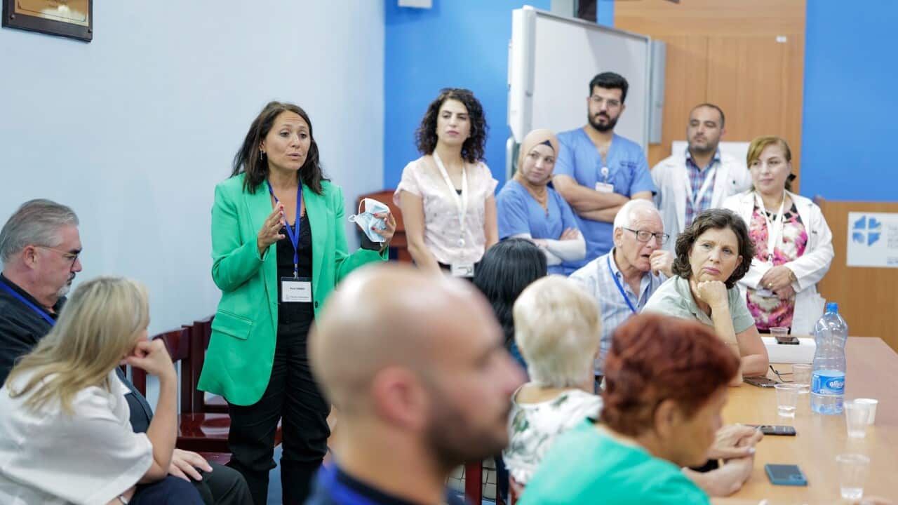 A woman in a green jacket speaks to a room of healthcare workers.