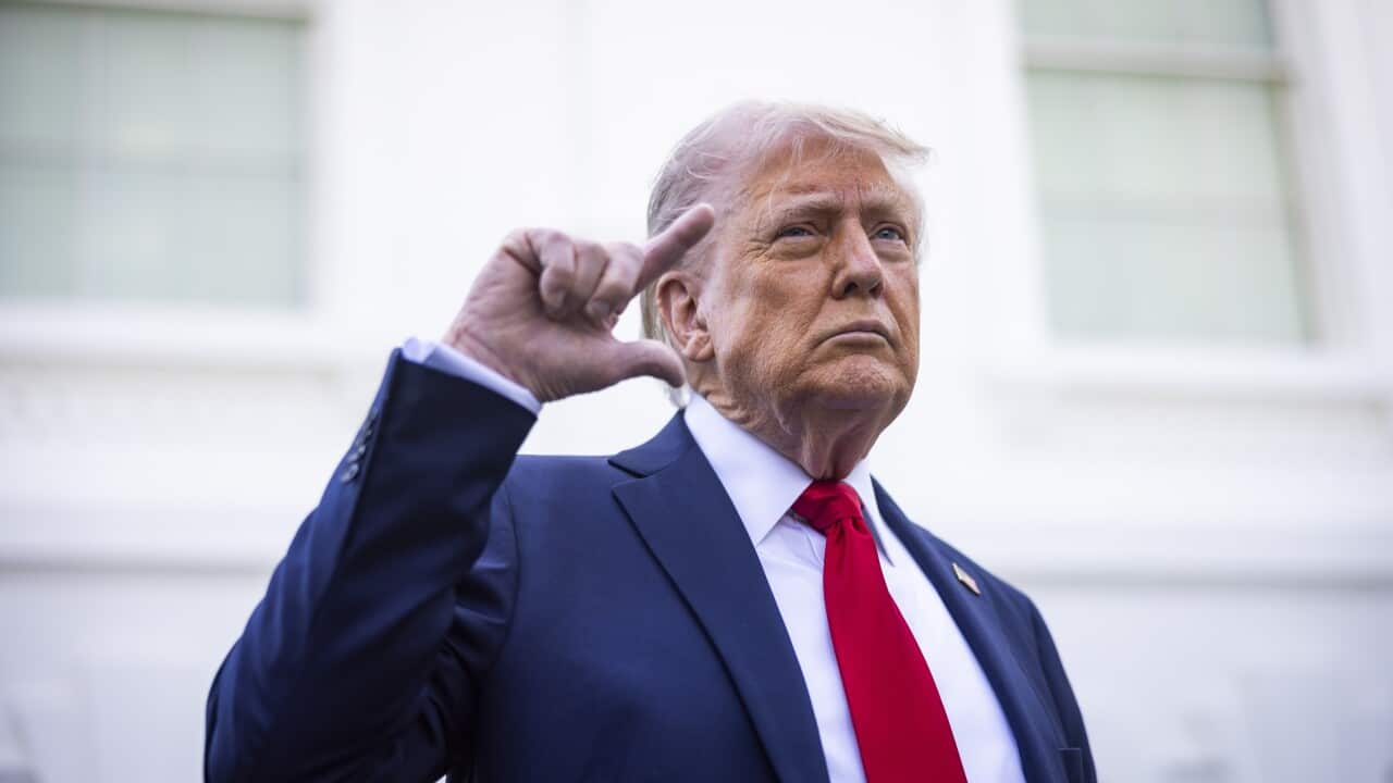 Donald Trump, in a blue suit and red tie, is gesturing with one hand.