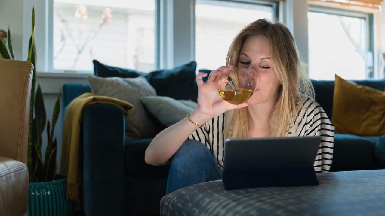 Woman drinking wine and looking at tablet at home