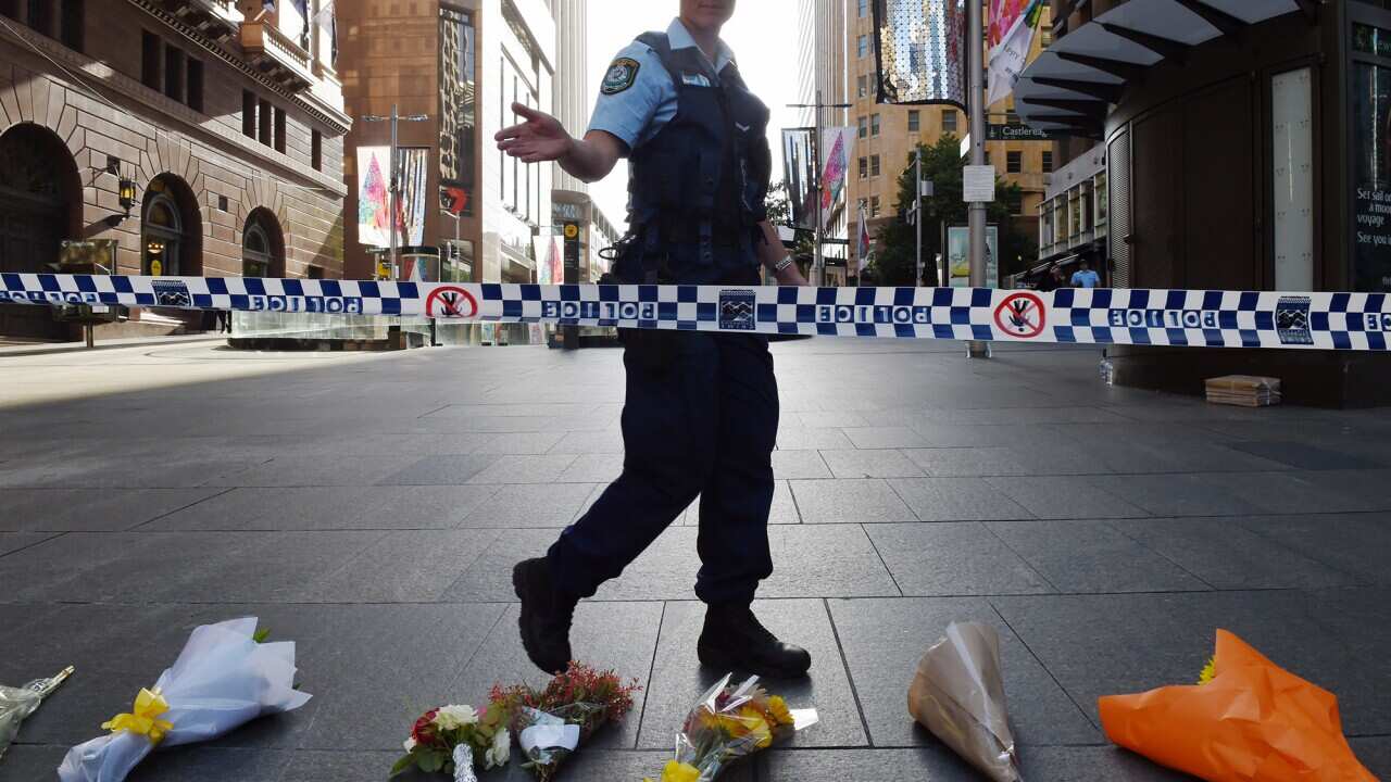 A police officer asks the media and onlookers to move back near flowers laid at the scene near the Lindt chocolate cafe in Martin Place following a siege, Sydney, Tuesday, Dec. 16, 2014.