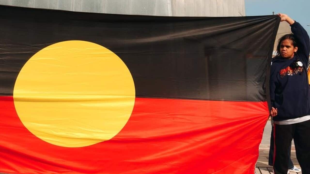 A girl holds the Aboriginal flag at a gathering in Federation Square