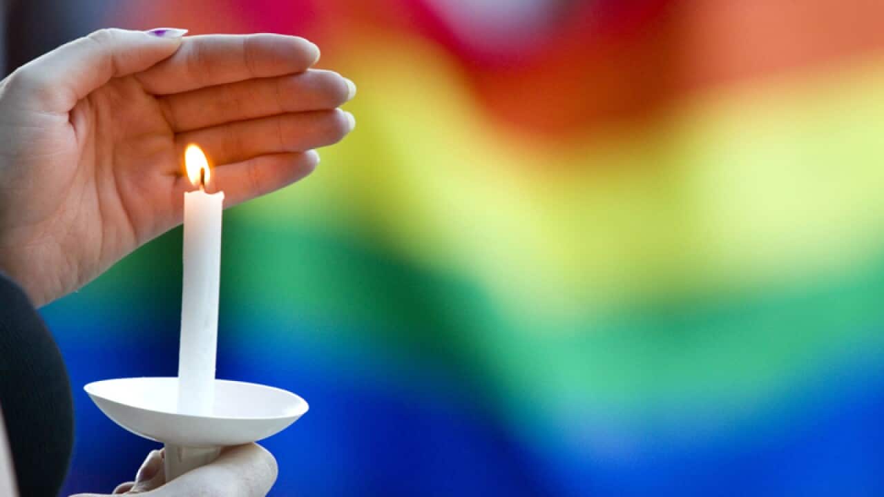 A candle burns in front of a pride flag during a vigil