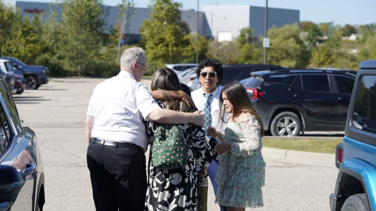 People appear distressed as they hug in a carpark.