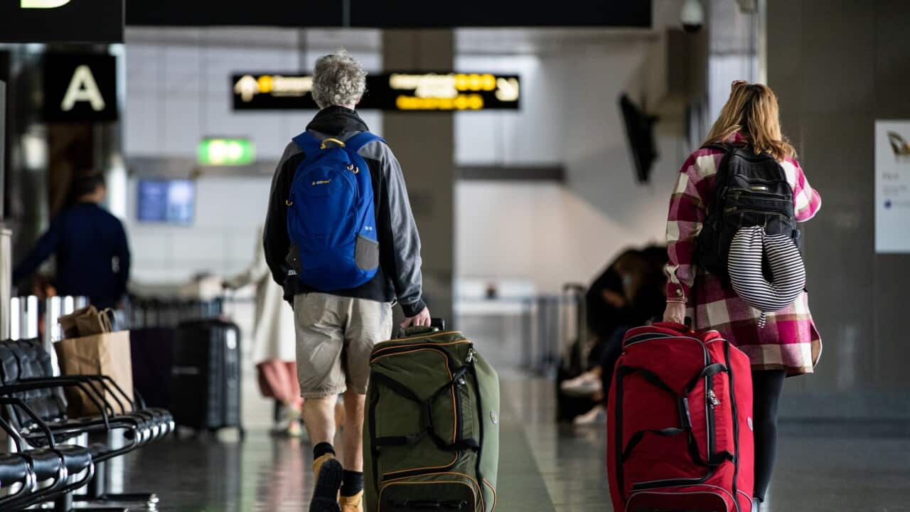 Two people with their backs to the camera, dragging their luggage behind them at the airport.
