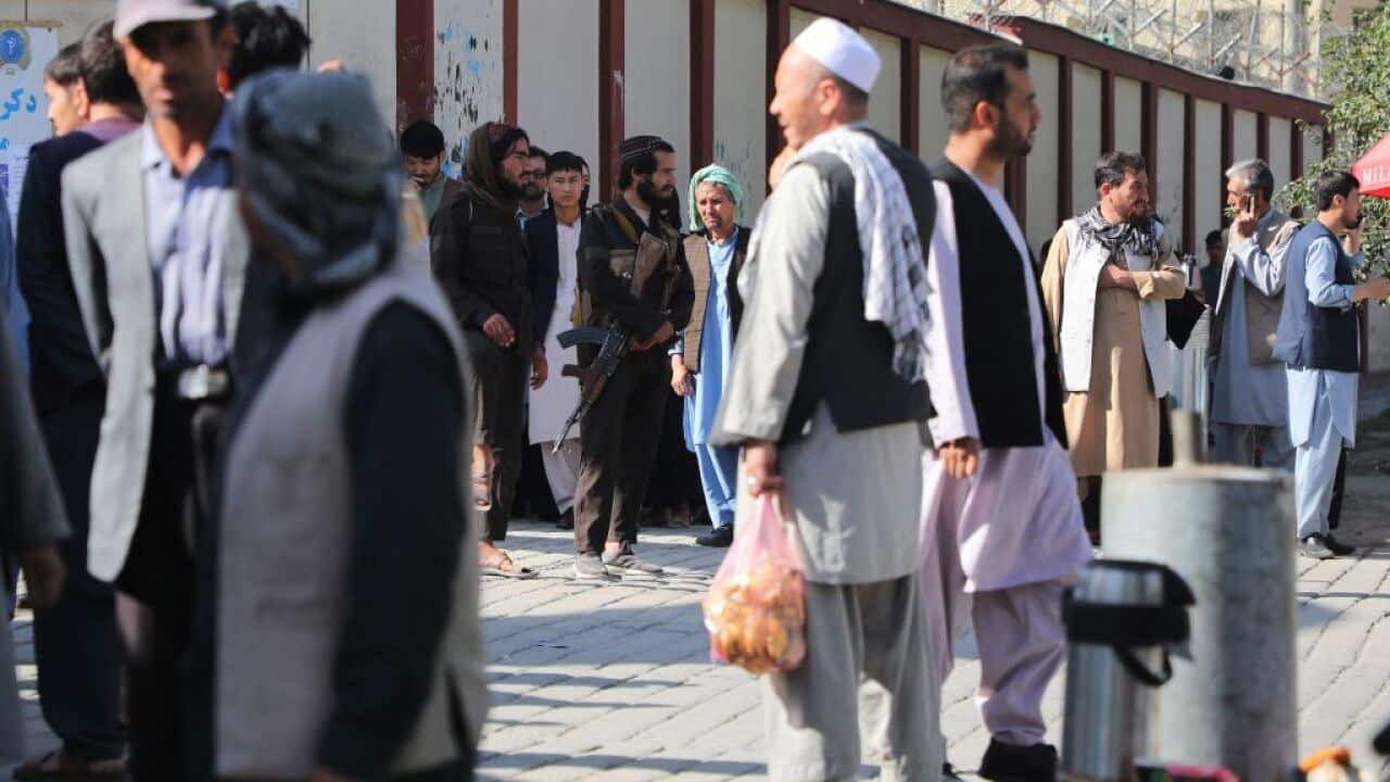 Taliban fighters are pictured standing guard as people gather to search for relatives following a blast in a learning centre in west Kabul.
