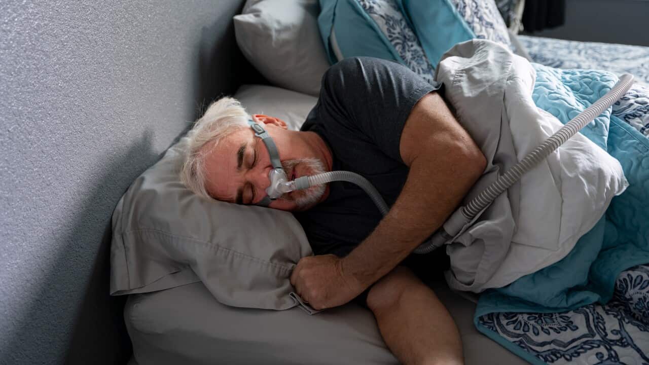 A 60-year-old man sleeps with a CPAP machine in bed to treat his sleep apnea, a condition where breathing repeatedly stops and starts during sleep.