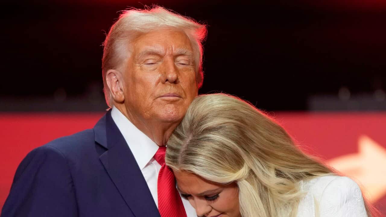 Donald Trump in a dark blue suit and red tie (left) comforts Erika Kirk, who is dressed in white and has her head against Trump's chest.