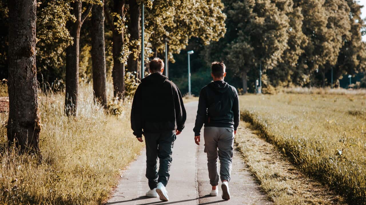 Two young men walking on a footpath outside facing away from camera