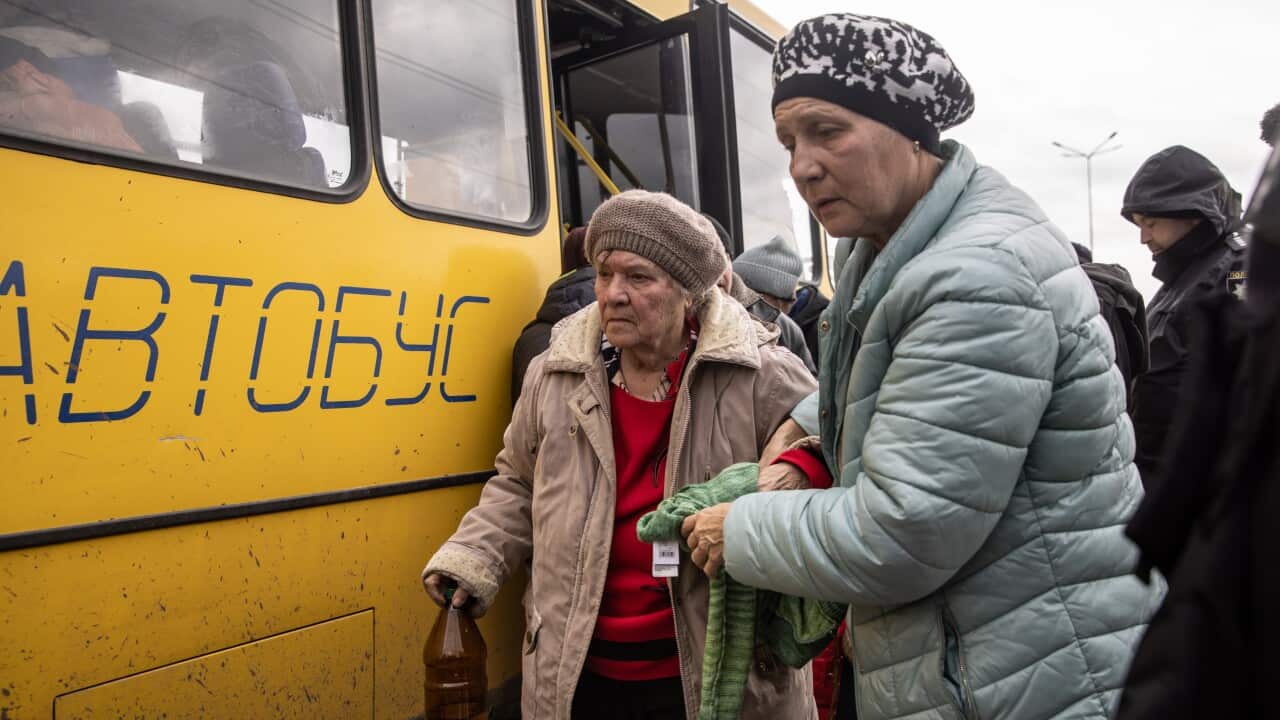 Two women get off a bus wearing layered clothing and warm hats.