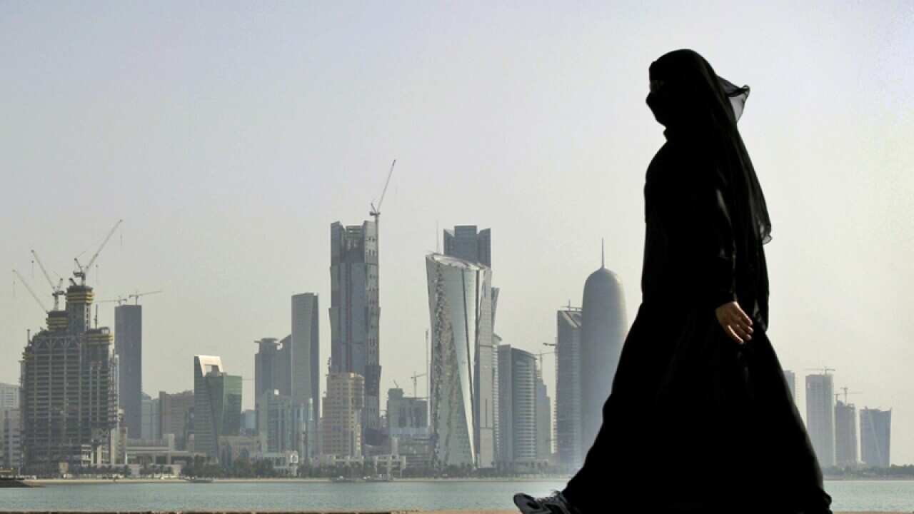 A Qatari woman walks in front of the city skyline in Doha