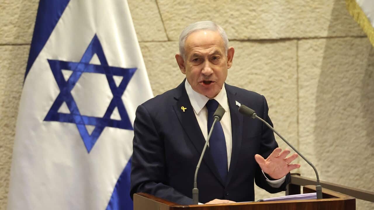 Benjamin Netanyahu, in a dark suit, is speaking into microphones as he stands in front of a lectern with an Israeli flag behind him.