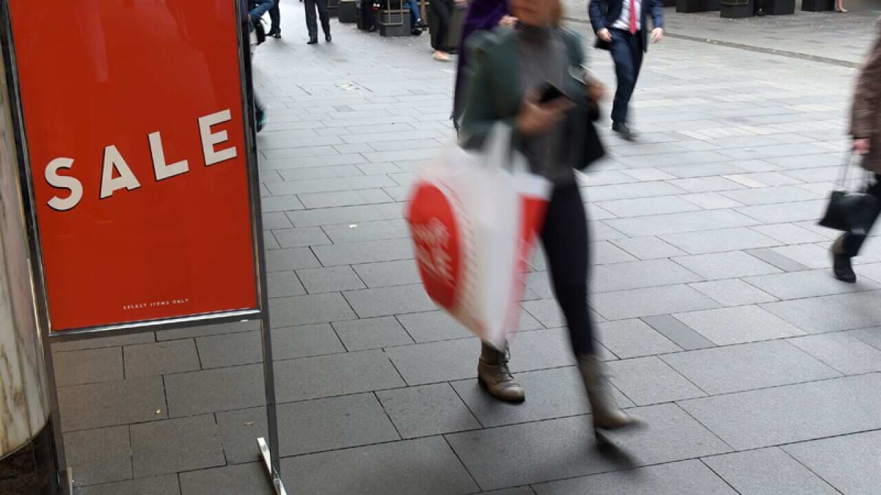 Pedestrians walk past a sale sign outside of a retail store in Sydney