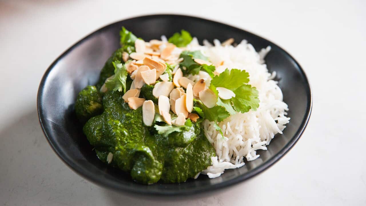 Bright green curry and white rice sit in a modern black bowl. The food is garnished with flaked almonds and coriander leaves.