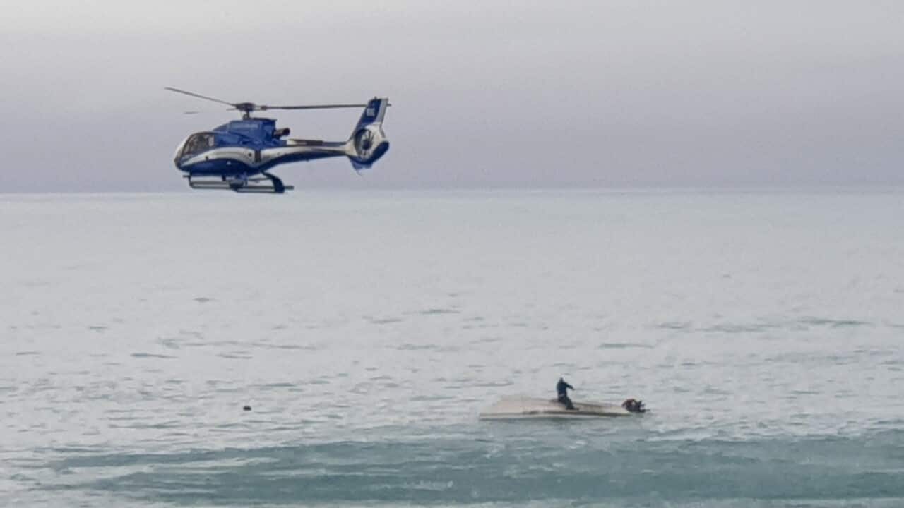 A helicopter flies overs an upturned boat with a survivor sitting on the hull off the coast of Kaikoura, New Zealand on 10 September 2022.