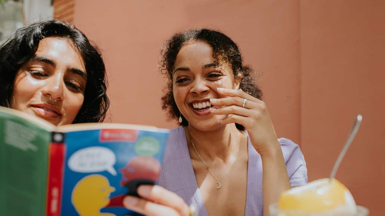 Two woman read and discuss a Italian language book on a terrace