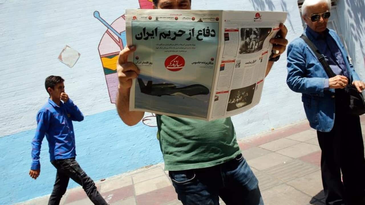 An Iranian man reads a newspaper about the shooting down of the drone
