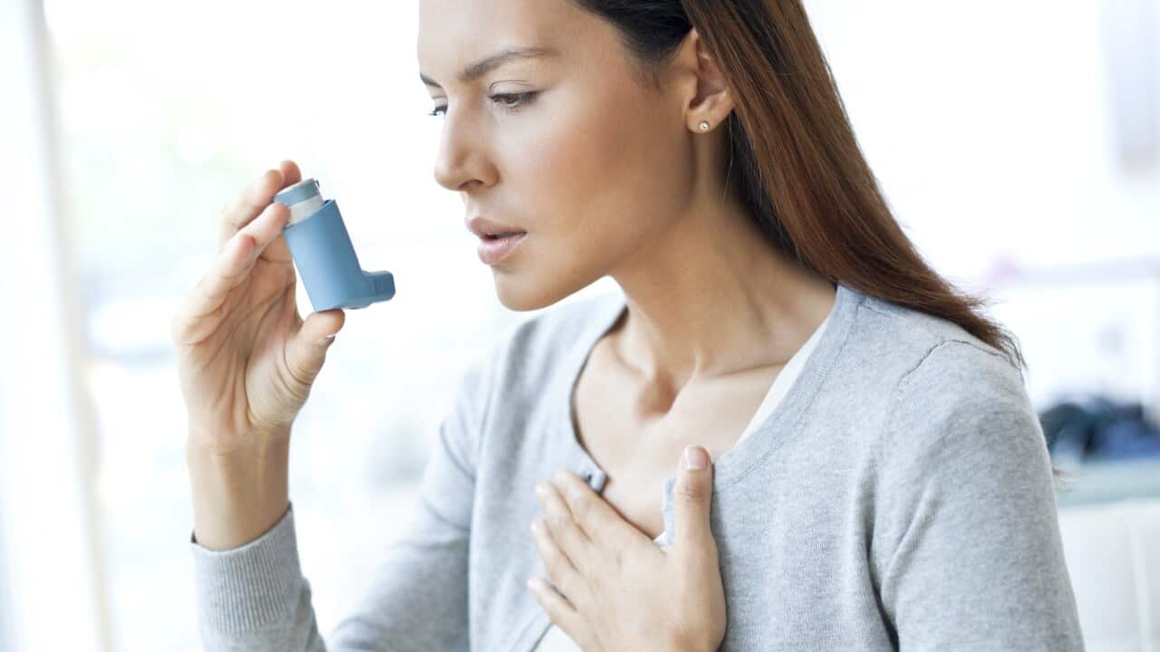 Young woman using inhaler touching chest