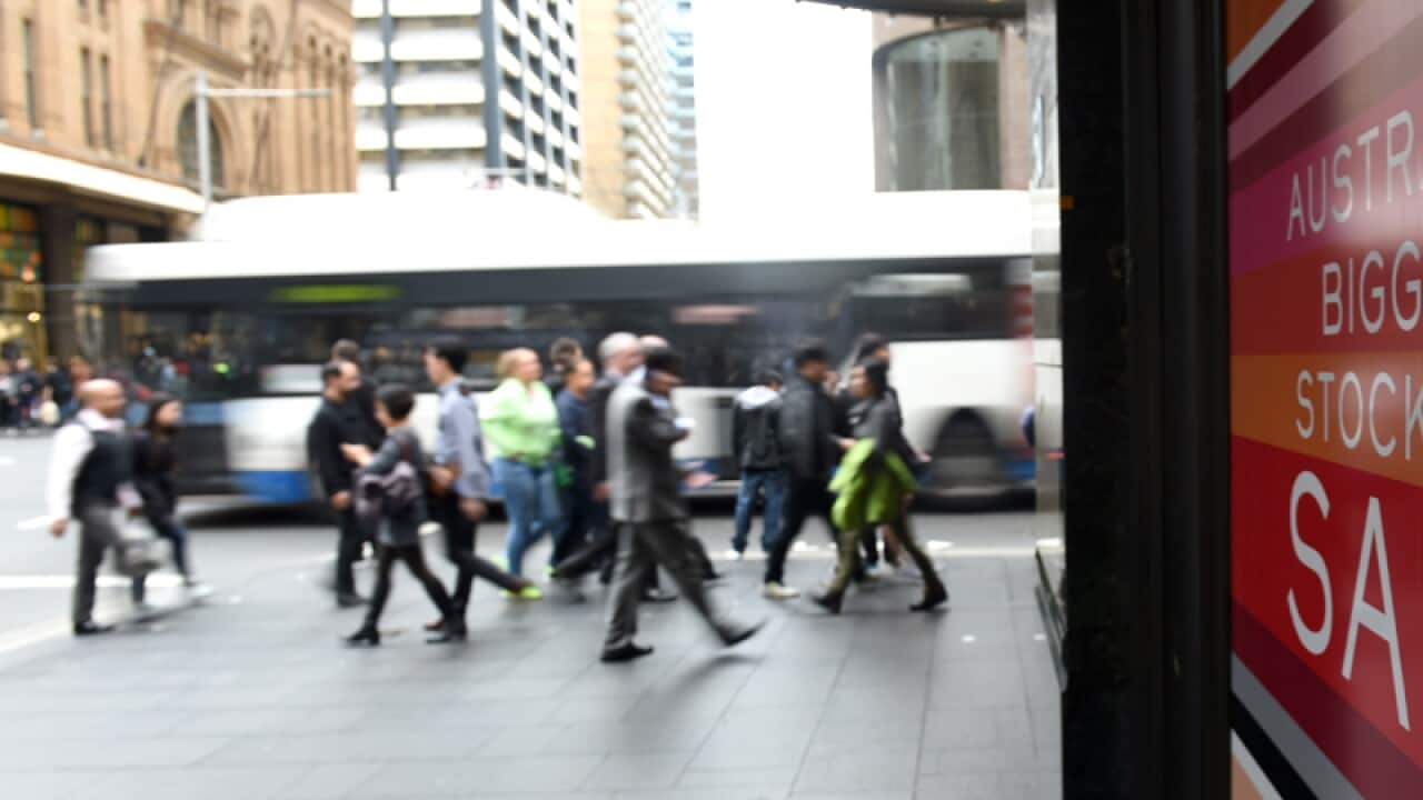 Pedestrians walk past a sale sign.